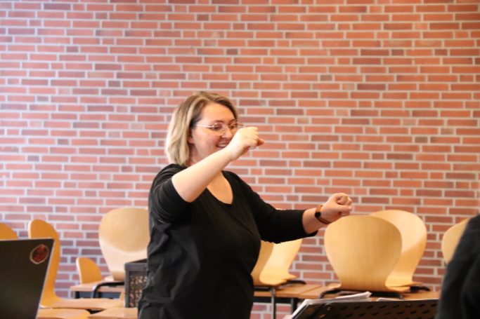 Frau steht in einem Raum mit Ziegelwand und erklärt etwas mit den Händen.
